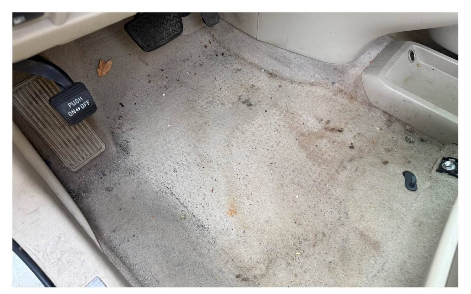 A stained, gritty driver's footwell before interior restoration